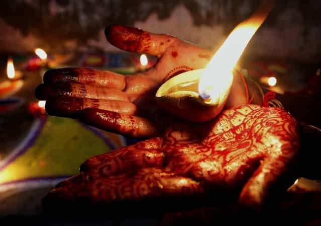 A Hindu girl holds an earthen lamp while decorating an area of her house to celebrate Diwali, the Hindu festival of lights, in Karachi, Pakistan, November 13, 2012. (Photo by Shakil Adil/Associated Press)