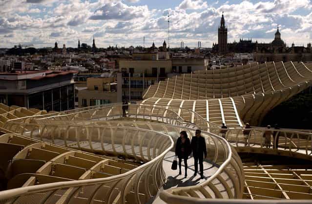 A couple walk along of one the corridors of the Metropol Parasol, overseeing the old city and the Giralda Cathedral of Seville, November 18, 2012. The Metropol Parasol by Jurgen Mayer H. Architects claims to be the world's largest wooden structure. (Photo by Emilio Morenatti/Associated Press)