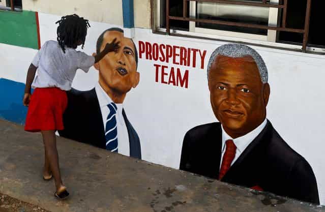 A girl touches a painted picture of President Barack Obama and Sierra Leone President Ernest Bai Koroma, on the outside of a hair salon, in Freetown, Sierra Leone, November 19, 2012. (Photo by Rebecca Blackwel/Associated Press)