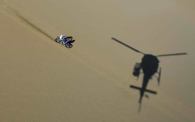 A helicopter casts a shadow on the ground as Yamaha rider David Casteu of France competes in the 2nd stage in Pisco, Peru. (Photo by Franck Fife/Associated Press)