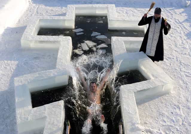A Belarus Orthodox believer plunges into icy waters as a priest blesses him on the eve of the Epiphany holiday in Pilnitsa some 30 km outside Minsk, on January 18, 2013. Thousands of believers jumpe into holes cut in ice, braving freezing temperatures, on January 18 and early on January 19 to mark Epiphany, when they take part in a baptism ceremony. (Photo by Viktor Drachev/AFP Photo)