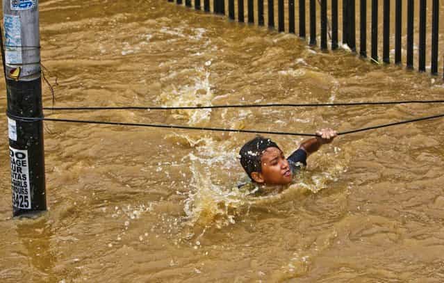 A man grabs wires to keep from being swept away by flood wates in Jakarta, Indonesia, January 18, 2013. Authorities were working to repair a dike that collapsed and flooded the Indonesian capital. (Photo by Tatan Syuflana/Associated Press)