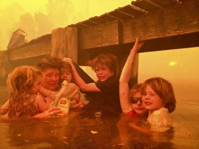 In this January 4, 2013, photo provided by the Holmes family, Tammy Holmes and her grandchildren take refuge under a jetty as a wildfire rages near them in Dunalley,Australia, on January 9, 2013. The family credits God with their survival from the fire that destroyed around 90 homes there. (Photo by Tim Holmes)