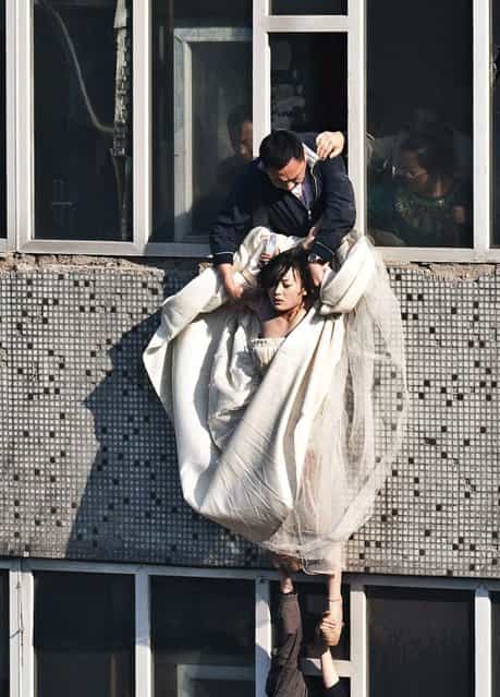 A 22-year-old woman in a wedding gown is grabbed by Guo Zhongfan, a local community officer, as she attempts to kill herself by jumping out of a seven-storey residential building in Changchun, Jilin province. According to local media, the woman tried to commit suicide after her boyfriend of four years broke up with her, just as they were making plans to get married. The woman did not sustain any injuries during the incident. (Photo by China Daily/Reuters)
