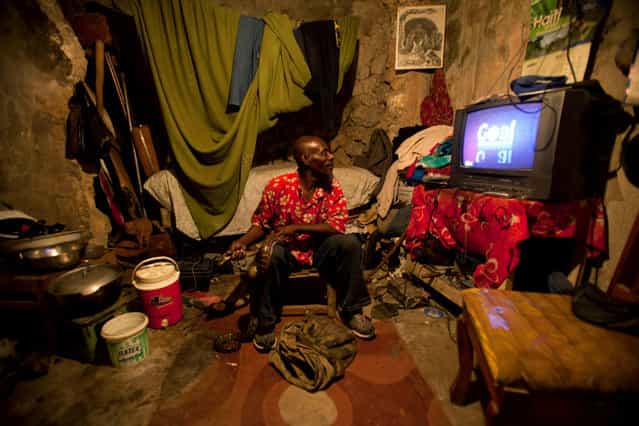 In this January 24, 2013 photo, snake handler Saintilus Resilus watches a soccer game at his home while holding a snake, and a bag of more snakes lays at his feet, as he prepares for his street performances using snakes, for which he charges money, in Petionville, Haiti. Resilus is one of millions of people scrambling to get by in a country where the unemployment rate hovers around 60 percent and most get by on $2 a day. (Photo by Dieu Nalio Chery/AP Photo/Matt Dayhoff)