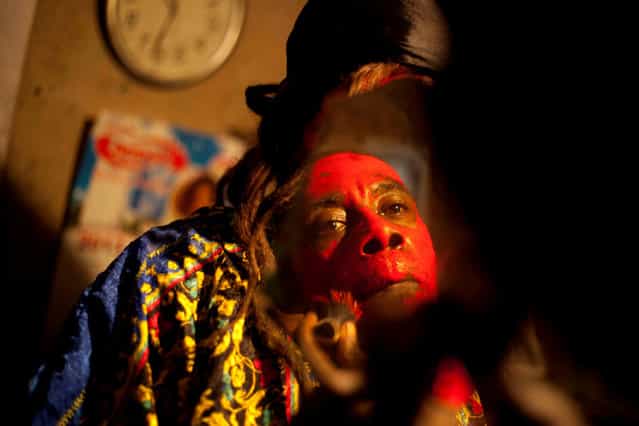 In this January 27, 2013 photo, snake handler Saintilus Resilus looks in the mirror as he paints his face red before performing with snakes for money during the pre-Lenten Carnival season at his home in Petionville, Haiti. It's the serpents that help him eat and pay rent, in addition to his work for a neighborhood herbologist. And it's the snakes for which he's most famous. (Photo by Dieu Nalio Chery/AP Photo/Matt Dayhoff)