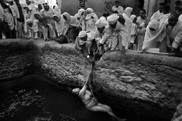 [Pilgrims gather to watch as an infertile worshiper is lowered into a baptism pool with a rope held by priests. According to local faith the holy water has fertility powers that will allow her to conceive. Every year, just before Christmas day, thousands of pious Christian orthodox worshipers make a pilgrimage to Lalibela, a small town in Ethiopia's highlands, known as Jerusalem of Africa or Black Jerusalem. Lalibela is famous for its 13th century monolithic churches, carved out of the living rock]. (Photo and comment by Gali Tibbon, Israel/2013 Sony World Photography Awards