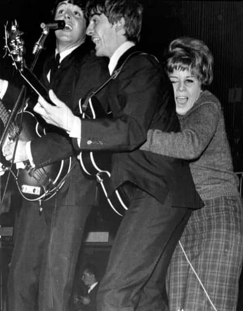 A young Swedish fan hugs George Harrison as The Beatles play at a pop festival in Stockholm, Sweden, on October 26, 1963. Paul McCartney, left, sings with Harrison. (Photo by AP Photo)