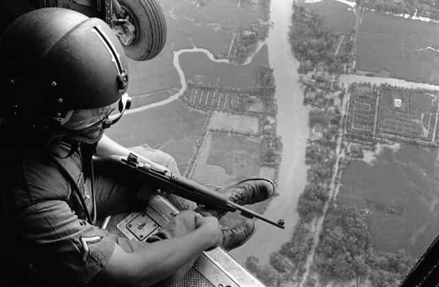 A Helmeted U.S. Helicopter Crewchief watches ground movements of Vietnamese troops from above during a strike against Viet Cong Guerrillas in the Mekong Delta Area, on January 2, 1963. The communist Viet Cong claimed victory in the continuing struggle in Vietnam after they shot down five U.S. helicopters. An American officer was killed and three other American servicemen were injured in the action. By 1963, nearly 16,000 American military personnel were deployed in South Vietnam. (Photo by AP Photo)