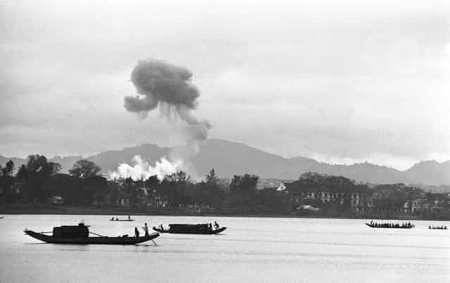 Napalm air strikes raise clouds of smoke into gray monsoon skies as houseboats glide down the Perfume River toward Hue in Vietnam, on February 28, 1963, where the battle for control of the old Imperial City has ended with a Communist defeat. Firebombs were directed against a village on the outskirts of Hue. (Photo by AP Photo)