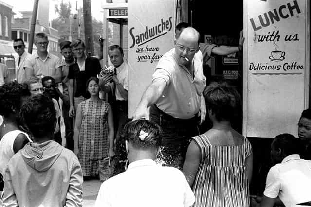 Robert Fahsenfeldt, owner of a segregated lunchroom in the racially tense Eastern Shore community of Cambridge, Maryland, douses a white integrationist with water, on July 8, 1963. The integrationist, Edward Dickerson, was among three white and eight African American protesters who knelt on the sidewalk in front of the restaurant to sing freedom songs. A raw egg, which Fahsenfeldt had broken over Dickerson's head moments earlier, still is visible on the back of Dickerson's head. The protesters were later arrested. (Photo by William A. Smith/AP Photo)