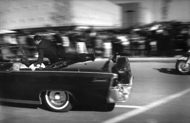 At 12:30 pm, just seconds after President John F. Kennedy and Texas Governor John Connally were shot in Dallas, Texas, the limousine carrying mortally wounded president races toward the hospital, on November 22, 1963. With secret service agent Clinton Hill riding on the back of the car, Mrs. John Connally, wife of the Texas governor, bends over her wounded husband, and Mrs. Kennedy leans over the president. (Photo by Justin Newman/AP Photo)