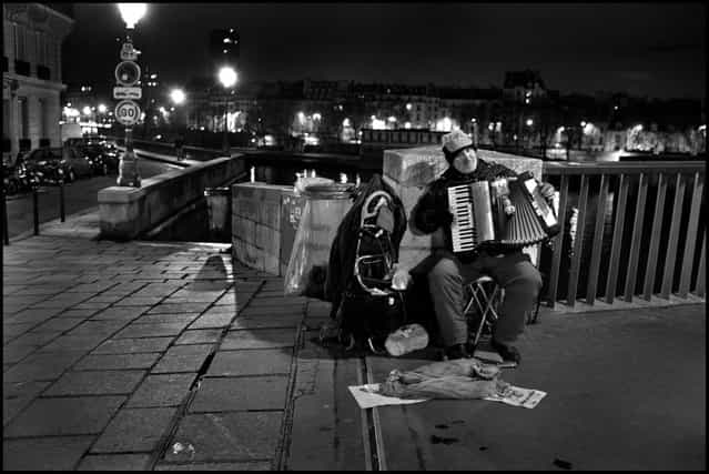 On a bridge in Paris on a cold November night, a lone man sits and plays a song. His song, is our song and our night is better for it. (Photo and comment by Peter Turnley)
