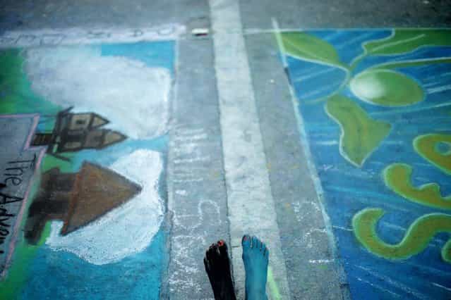 Kaiden Buscemi of Lake Worth sits amid paintings by Palm Beach Maritime Academy students on Saturday. She and other children painted not only the street but themselves during the festival. (Photo by Thomas Cordy/The Palm Beach Post)