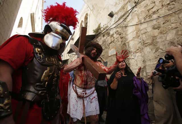 A man playing the role of Jesus carries a cross to the Church of the Holy Sepulchre on Good Friday during Holy Week, in Jerusalem's Old City March 29, 2013. Christian worshippers retraced the route Jesus took along Via Dolorosa to his crucifixion in the Church of the Holy Sepulchre. Holy Week is celebrated in many Christian traditions during the week before Easter. (Photo by Baz Ratner/Reuters)