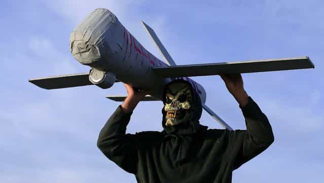 John Amidon holds up a model of an Air Force drone while protesting outside Creech Air Force Base in Indian Springs, Nevada, on March 27, 2013. Amidon is part of the Nevada Desert Experience group which holds an annual peace walk protesting the use of drones and nuclear weapons. The walk, which lasts five days, starts from Las Vegas, makes a stop at Creech Air Force Base and ends at the Nevada National Security Site in Mercury, Nevada. (Photo by Julie Jacobson/Associated Press)