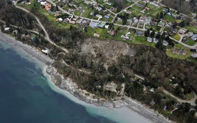 In this aerial photo, a landslide is shown near Coupeville, Wash. on Whidbey Island, Wednesday, March 27, 2013. Whidbey Island authorities say one home has been severely damaged by the landslide that has isolated or threatened 33 more homes in the community overlooking Puget Sound about 50 miles north of Seattle. Central Whidbey Fire and Rescue evacuated one person from the damaged home. About 10 more residents have been evacuated by boat. (Photo by Ted S. Warren/AP Photo)