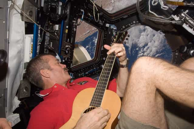 Canadian Space Agency astronaut Chris Hadfield strums his guitar in the ISS's Cupola on December 25, 2012. Hadfield, a long-time member of an astronaut band called Max Q, later joined with the other five Expedition 34 crew members in a more spacious location to provide an assortment of Christmas carols for the public. (Photo by NASA/The Atlantic)