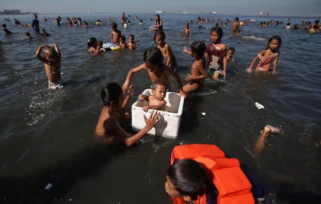 A Filipino boy rides inside a styrofoam box as they swim at the polluted waters of Manila's bay, Philippines as they celebrate Easter Sunday, March 31, 2013. Despite a city-imposed swimming ban, many poor Filipinos set up makeshift tents and swam along the bay to cool themselves from summer's sweltering heat. (Photo by Aaron Favila/AP Photo)