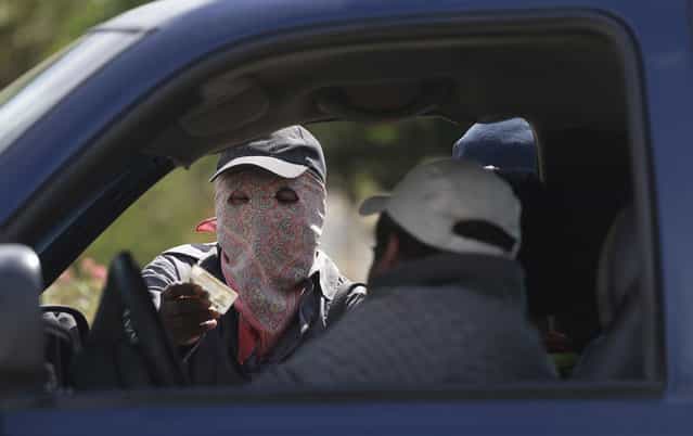 A masked armed man checks the identity of a driver at a roadblock at the entrance to the town of El Pericon, near Ayutla, Mexico, on January 18, 2013. Hundreds of men in the southern Mexico state of Guerrero have taken up arms to defend their villages against drug gangs, a vigilante movement born of frustration at extortion, killings and kidnappings that local police are unable, or unwilling, to stop. (Photo by Dario Lopez-Mills/AP Photo /The Atlantic)
