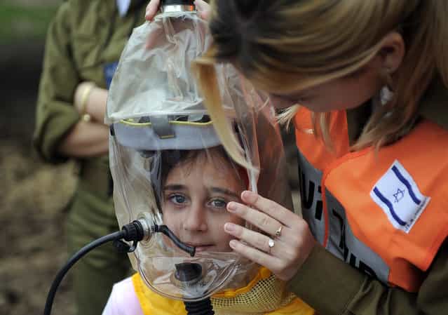An Israeli soldier instructs children on how to wear a gas mask during an emergency drill simulating a rocket attack in the central town of Kiryat Malachi, on February 14, 2013. (Photo by David Buimovitch/AFP Photo /The Atlantic)