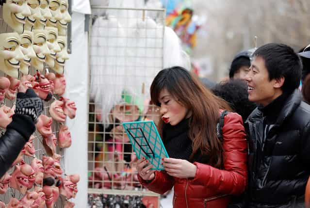 A woman tries on masks at a Spring Festival Temple Fair for celebrating Chinese Lunar New Year, on February 11, 2013 in Beijing, China. (Photo by Lintao Zhang /The Atlantic)