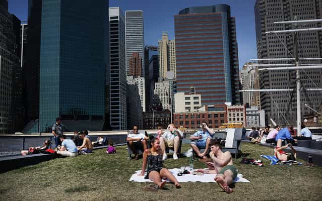 People relax along the East River in lower Manhattan during warm weather on April 9, 2013 in New York City. For the first time since October, temperatures are expected to rise above 70 degrees this week in New York and surrounding areas. (Photo by Spencer Platt/AFP Photo)