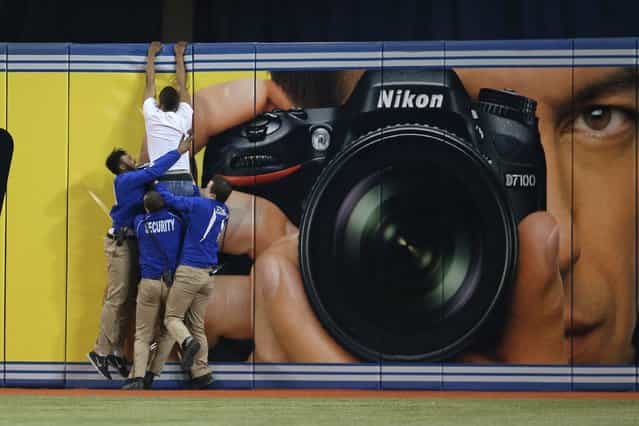 A trespasser tries to jump the outfield wall as security guards pull him down during the Toronto Blue Jays MLB game against the Boston Red Sox on April 7, 2013 at Rogers Centre in Toronto, Ontario, Canada. (Photo by Tom Szczerbowski/AFP Photo)