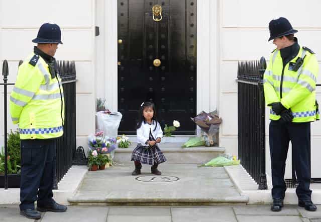 British police look on as a girl holds a rose amid floral tributes at the home of former British Prime Minister Margaret Thatcher in central London on April 10, 2013. British lawmakers will interrupt their holidays for a special session of parliament on April 10 to debate the legacy of Margaret Thatcher, who died on April 8 aged 87 after suffering a stroke. (Photo by Leon Neal/AFP Photo)