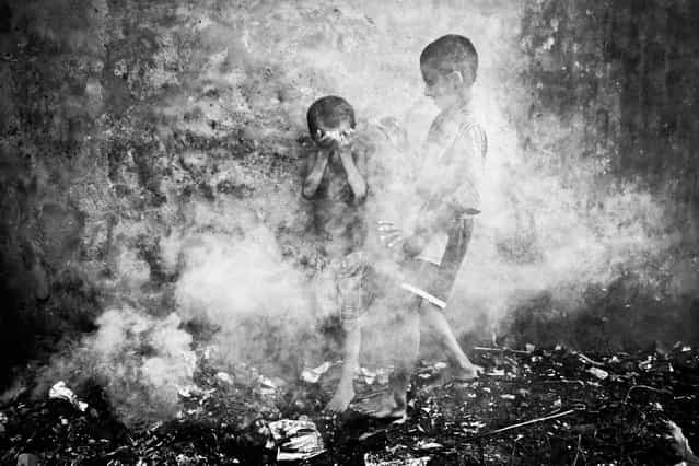 Two homeless street children were playing in the smoke created from burnt straws at Chittagong, Bangladesh. Suddenly dense smoke covered them and they were trying to protect themselves and escape. (Photo by Kazi Riasat Alve/2013 Sony World Photography Awards)