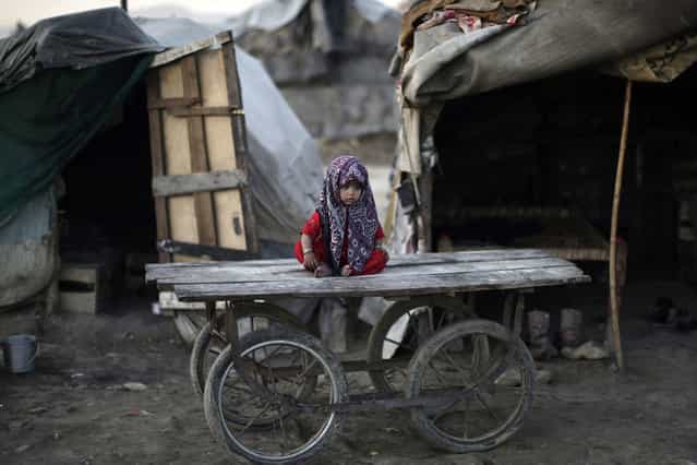 A Pakistani child, whose family was displaced by 2010 floods from a village in Pakistan's Sindh province, sits on a wooden cart outside her family's makeshift home, in a slum on the outskirts of Islamabad, on February 8, 2013. (Photo by Muhammed Muheisen/AP Photo)