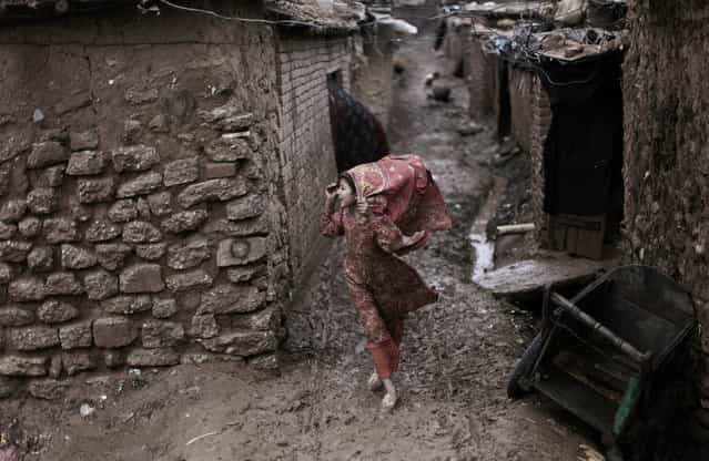 An Afghan refugee girl holds on to her headscarf against the wind while making her way along a muddy alley of a slum during a rainy day, on the outskirts of Islamabad, on February 4, 2013. (Photo by Muhammed Muheisen/AP Photo)