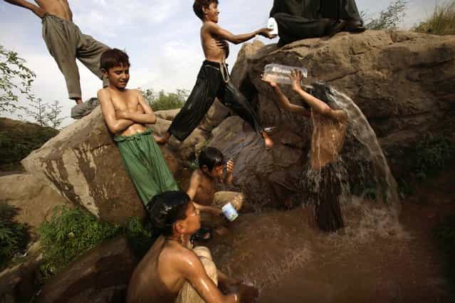 Pakistani boys, who make a living by collecting recyclable materials and selling them to a recycling factory, shower in a pool of water created by a broken water pipe following their daily work, on a roadside on the outskirts of Islamabad, Pakistan, Tuesday, April 17, 2012. (Photo by Muhammed Muheisen/AP Photo)