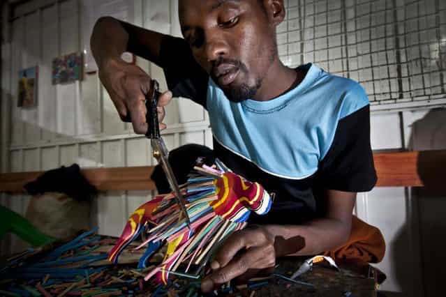 In this photo taken Monday, April 29, 2013, carver Daniel Lekalau, 26, uses scissors to trim the mane of a toy lion he is making from pieces of discarded flip-flops, at the Ocean Sole flip-flop recycling company in Nairobi, Kenya. The company is cleaning the East African country's beaches of used, washed-up flip-flops and the dirty pieces of rubber that were once cruising the Indian Ocean's currents are now being turned into colorful handmade giraffes, elephants and other toy animals. (Photo by Ben Curtis/AP Photo)