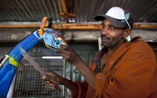 In this photo taken Monday, April 29, 2013, Jackson Mbatha, 40, uses a knife to carve part of the neck of a large giraffe he is making from pieces of discarded flip-flops, at the Ocean Sole flip-flop recycling company in Nairobi, Kenya. The company is cleaning the East African country's beaches of used, washed-up flip-flops and the dirty pieces of rubber that were once cruising the Indian Ocean's currents are now being turned into colorful handmade giraffes, elephants and other toy animals. (Photo by Ben Curtis/AP Photo)