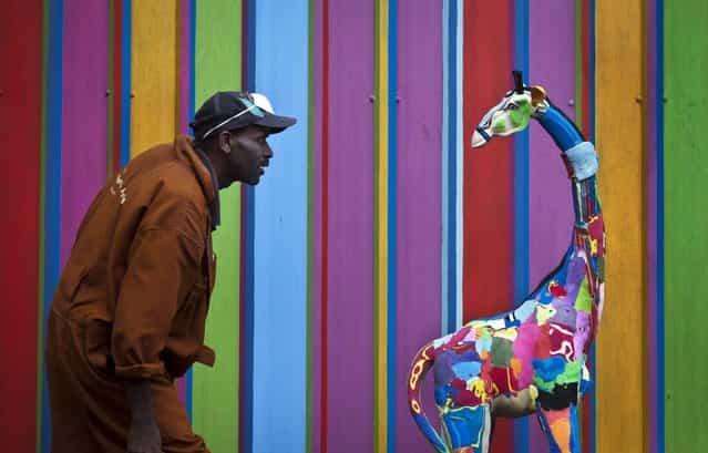In this photo taken Monday, April 29, 2013, carver Jackson Mbatha, 40, poses next to a an unfinished large toy giraffe he is making from pieces of discarded flip-flops, in front of a painted workshop wall at the Ocean Sole flip-flop recycling company in Nairobi, Kenya. The company is cleaning the East African country's beaches of used, washed-up flip-flops and the dirty pieces of rubber that were once cruising the Indian Ocean's currents are now being turned into colorful handmade giraffes, elephants and other toy animals. (Ben Curtis/AP Photo)