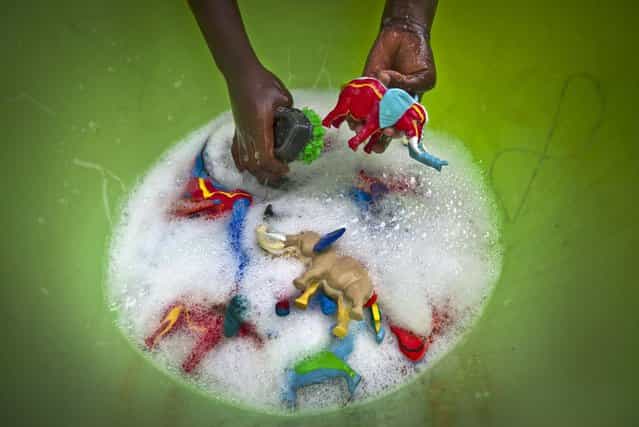 In this photo taken Monday, April 29, 2013, a female worker washes some finished toy animals made from pieces of discarded flip-flops, in a bucket at the Ocean Sole flip-flop recycling company in Nairobi, Kenya. The company is cleaning the East African country's beaches of used, washed-up flip-flops and the dirty pieces of rubber that were once cruising the Indian Ocean's currents are now being turned into colorful handmade giraffes, elephants and other toy animals. (Photo by Ben Curtis/AP Photo)