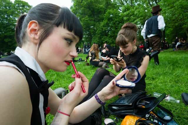 Two girls in black clothing refresh their make-up during the traditional park picnic on the first day of the annual Wave-Gotik Treffen, or Wave and Goth Festival, on May 17, 2013 in Leipzig, Germany. The four-day festival, in which elaborate fashion is a must, brings together over 20,000 Wave, Goth and steam punk enthusiasts from all over the world for concerts, readings, films, a Middle Ages market and workshops. (Photo by Marco Prosch)