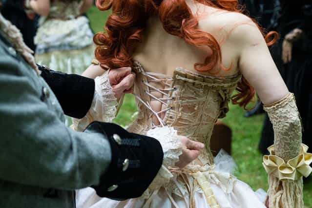 A man helps a woman straightening her corset during the traditional park picnic on the first day of the annual Wave-Gotik Treffen, or Wave and Goth Festival, on May 17, 2013 in Leipzig, Germany. The four-day festival, in which elaborate fashion is a must, brings together over 20,000 Wave, Goth and steam punk enthusiasts from all over the world for concerts, readings, films, a Middle Ages market and workshops. (Photo by Marco Prosch)