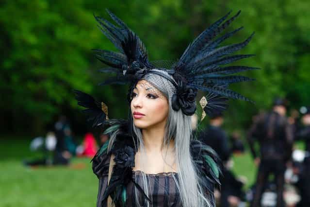 A woman in black clothing wearing a feather-hat poses for pictures during the traditional park picnic on the first day of the annual Wave-Gotik Treffen, or Wave and Goth Festival, on May 17, 2013 in Leipzig, Germany. The four-day festival, in which elaborate fashion is a must, brings together over 20,000 Wave, Goth and steam punk enthusiasts from all over the world for concerts, readings, films, a Middle Ages market and workshops. (Photo by Marco Prosch)
