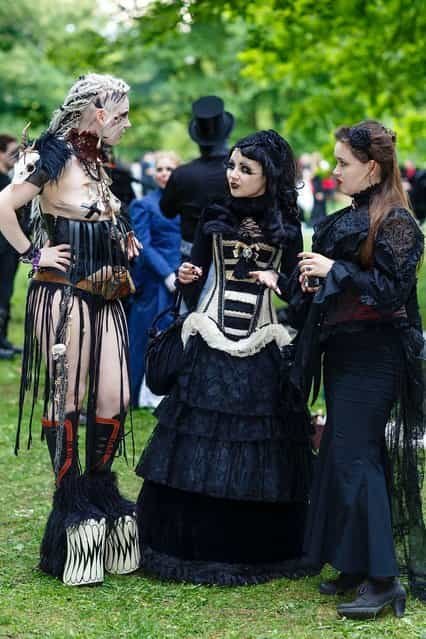 Three women in Victorian-style clothing chat during the traditional park picnic on the first day of the annual Wave-Gotik Treffen, or Wave and Goth Festival, on May 17, 2013 in Leipzig, Germany. The four-day festival, in which elaborate fashion is a must, brings together over 20,000 Wave, Goth and steam punk enthusiasts from all over the world for concerts, readings, films, a Middle Ages market and workshops. (Photo by Marco Prosch)