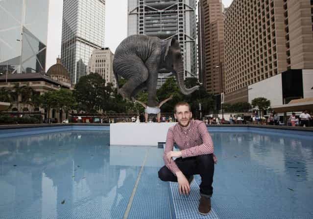 Contemporary French artist Fabien Merelle poses for photographers in front of his creation in five meters high sculpture [Pentateuque] in Central, business district of Hong Kong Tuesday, May 21, 2013. The artwork brings to real life the fantastical and seemingly impossible act of an average man balancing a gigantic elephant. The elephant and the man are modeled on one at the Singapore Zoo and on the artist himself. (AP Photo/Kin Cheung)
