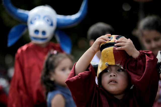 A child looks out from under his mask during the [Cavalhadas] festival in Pirenopolis, Brazil, Sunday, May 19, 2013. The popular festival, featuring masked horsemen, is a tradition that was introduced in the 1800's by a Portuguese priest to mark the the ascension of Christ. The 3-day festival reenacts the Christian knights' medieval defeat of the Moors. (Photo by Eraldo Peres/AP Photo)