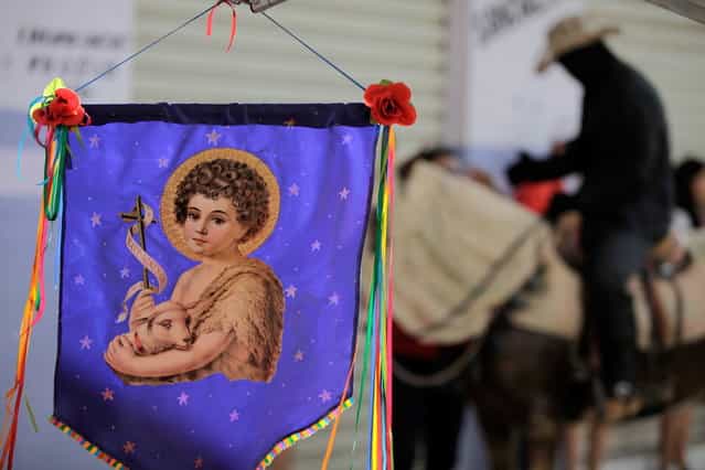 A banner of St John the Baptist hangs from the storefront of an artisan shop in Pirenopolis, Brazil, during the annual [Cavalhadas] festival, Sunday, May 19, 2013. The popular festival, featuring masked horsemen, is a tradition that was introduced in the 1800's by a Portuguese priest to mark the the ascension of Christ. The 3-day festival reenacts the Christian knights' medieval defeat of the Moors. (Photo by Eraldo Peres/AP Photo)