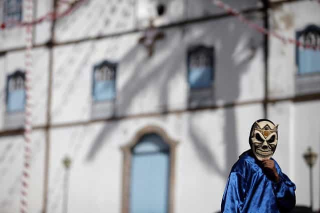 A masked boy walks past Our Lady of the Rosary church, during the [Cavalhadas] festival, in Pirenopolis, Brazil, Sunday, May 19, 2013. The popular festival is a tradition that was introduced in the 1800's by a Portuguese priest to mark the the ascension of Christ. The 3-day festival reenacts the Christian knights' defeat of the Moors. (Photo by Eraldo Peres/AP Photo)
