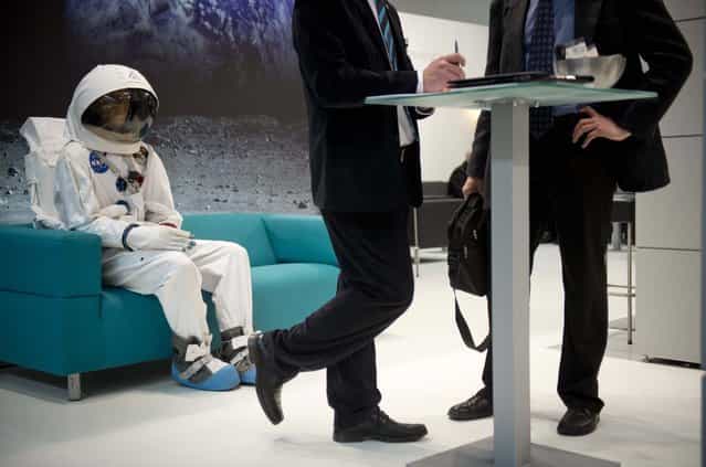 An astronaut is seen sitting on the couch behind two business men at the Wittenstein booth at the Hanover industrial fair on April 8, 2013 in Hanover, central Germany. (Photo by Odd Andersen/AFP Photo)