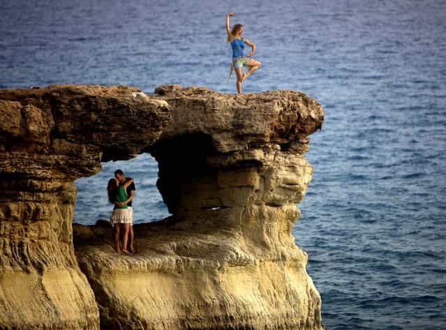 A couple kiss, as another tourist poses for photographs, at [The Caves] cliffs situated along the Mediterranean Sea on the southeast coast of Cyprus. (Photo by Patrick Baz/AFP Photo)