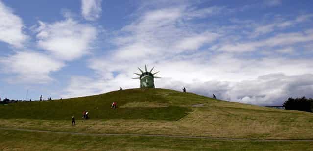Passersby walk toward a full-scale balloon replica of the Statue of Liberty head shortly after its inflation in Seattle's Gas Works Park. (Photo by Elaine Thompson/Associated Press)