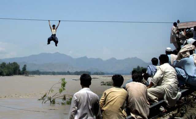 Onlookers perched on a damaged bridge watch a flood survivor climb a rope to cross the river in Pakistan's Swat Valley's Chakdara on August 3, 2010. (Photo by AFP Photo)