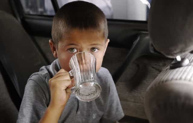 A boy drinks a glass of water given him by his grandmother on a 108F (42C) day. According to one guidebook [only the insane or deeply unfortunate] end up in Ashgabat in the hottest months of July and August. (Photo by Amos Chapple via The Atlantic)